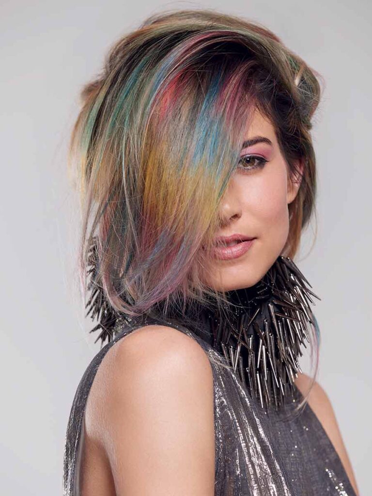 Porträt eines Models mit kurzem, asymmetrischem Haarschnitt und mehrfarbigen Strähnen in Blau-, Rot- und Goldtönen.