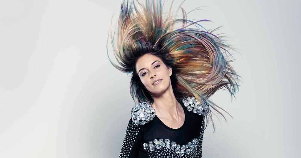 Model in Bewegung mit dynamisch aufgeworfenem Haar, farbige Strähnen in intensiven Kontrasten.