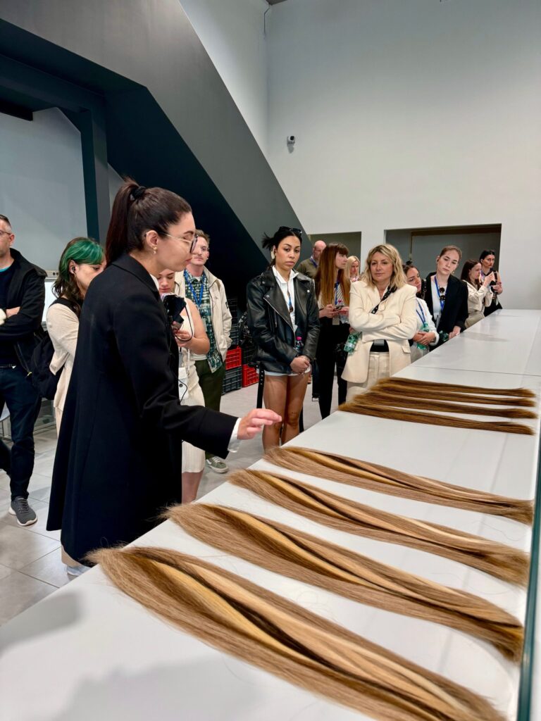 Italienische Mitarbeiterin erklärt Besucherinnen die Produktionsschritte anhand ausgelegter Haarsträhnen.