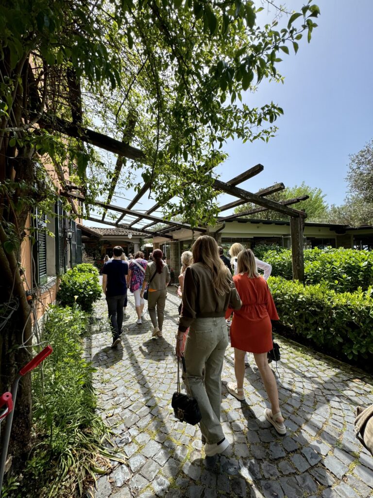 Teilnehmerinnen spazieren über einen schattigen Weg durch eine Gartenanlage auf dem Weg zum Mittagessen am See.