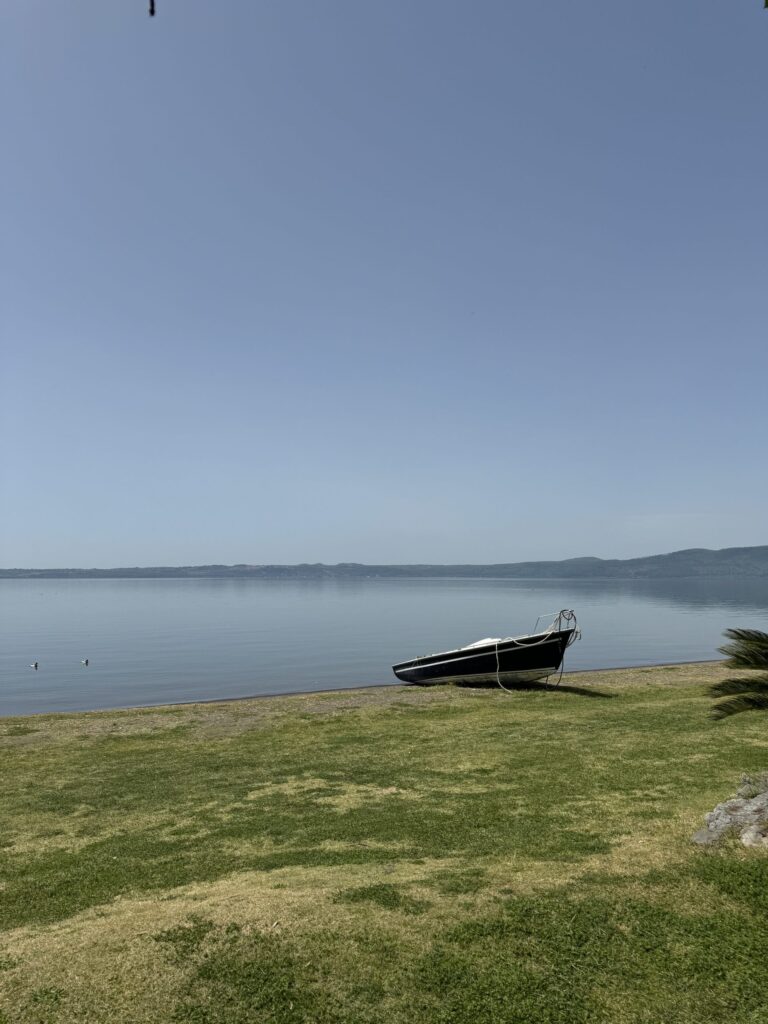 Ruhiger See mit kleinem Boot am Ufer unter blauem Himmel, Ort der gemeinsamen Mittagspause nahe Nepi.