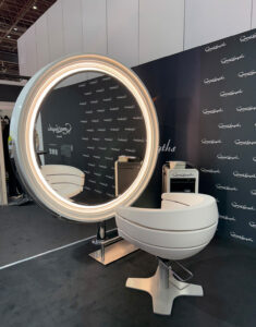 Moderner Friseurarbeitsplatz am Great-Lengths-Messestand mit beleuchtetem Rundspiegel, Friseurstuhl.