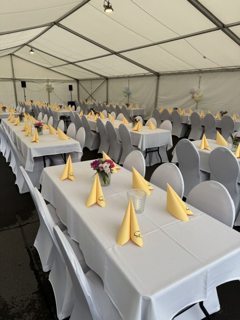 Gäste sitzen an langen Tischen im Festzelt und unterhalten sich