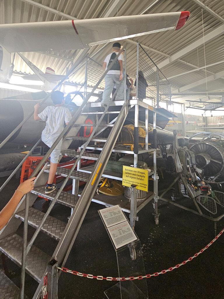 Kinder steigen über eine Metalltreppe, im Hintergrund sind ein Propellerflugzeug.